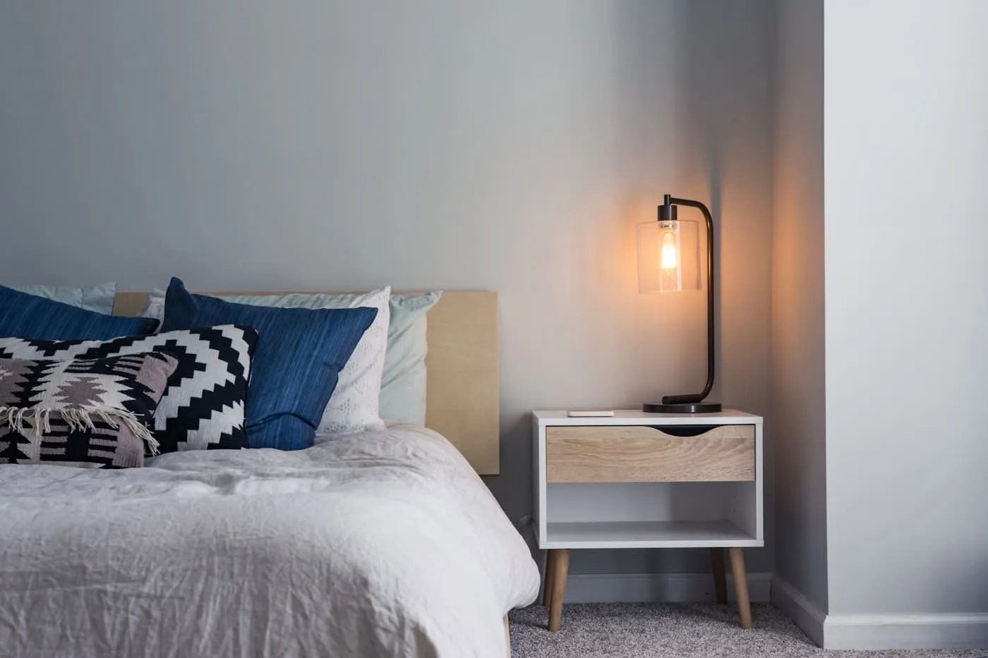 Layered coastal bed with white linen quilt, natural cushions, and rattan bedside table